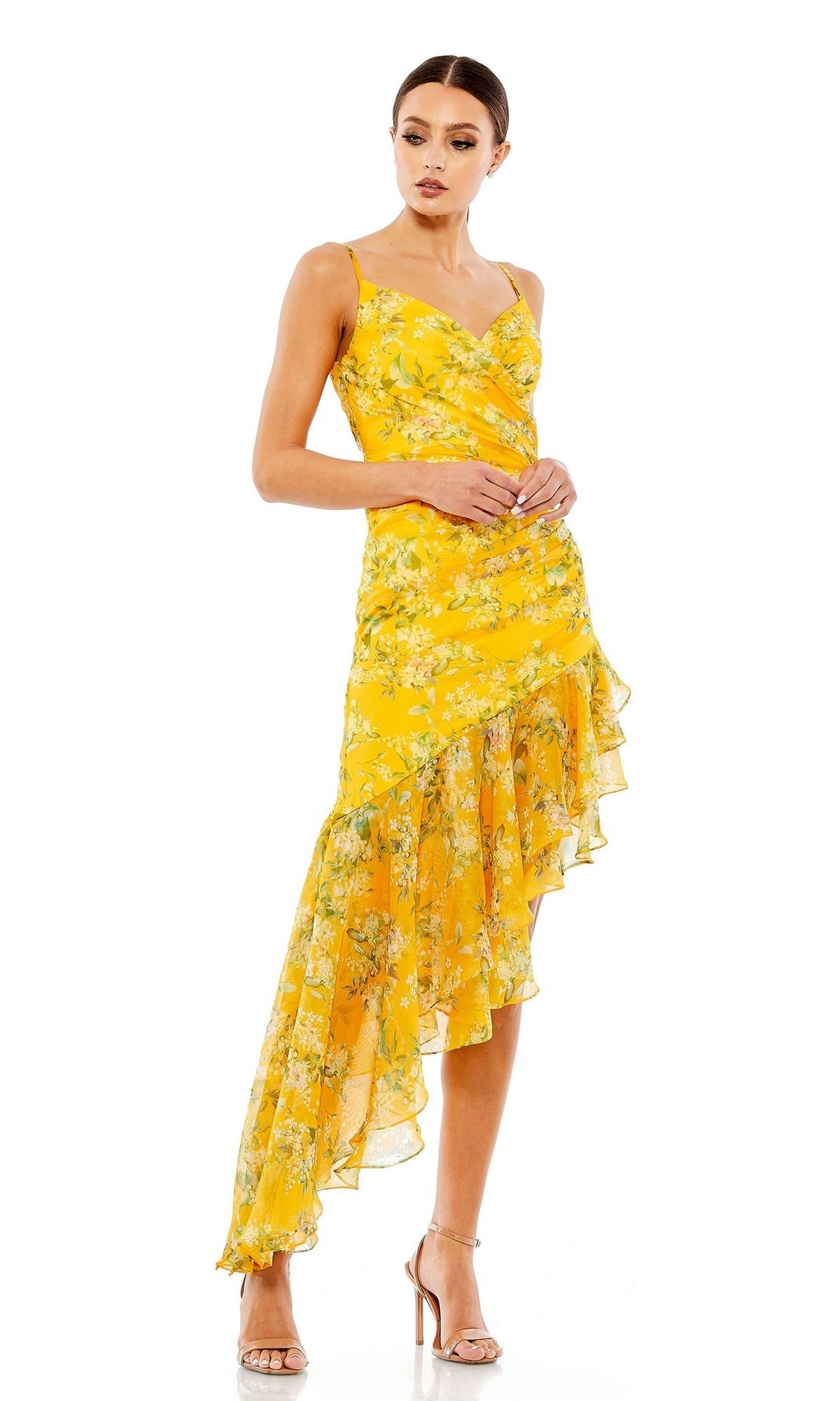 A woman in a Mac Duggal 70202 Yelow Print High-Low Party Dress with spaghetti straps and high-heeled sandals stands against a white background.